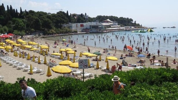 Une plage avec de nombreux parasols jaunes et des chaises longues, un ciel dégagé et un bâtiment en arrière-plan.