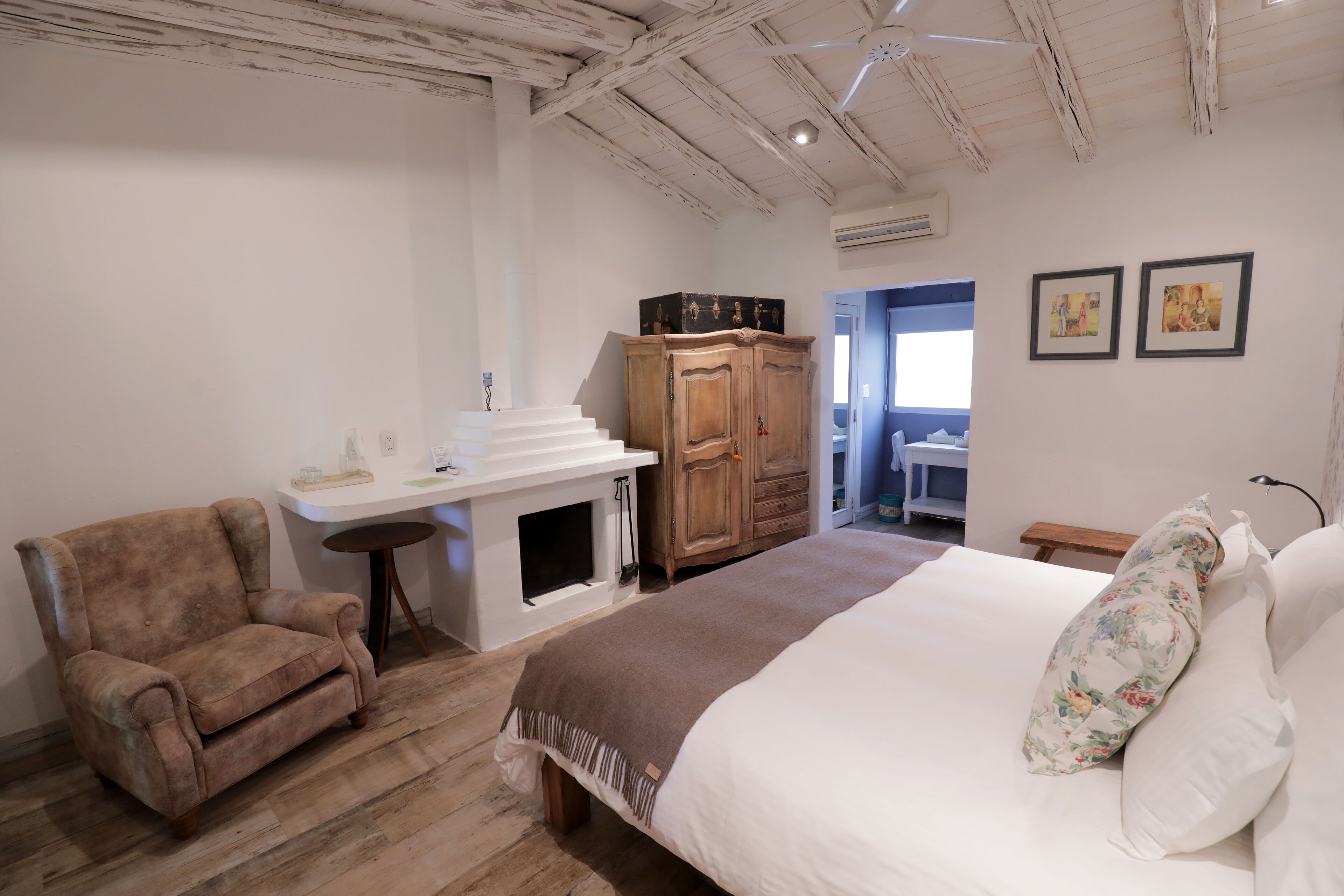 A bedroom with a large bed, a wooden wardrobe, a small table, and a chair.