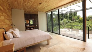 A modern bedroom with a wooden ceiling, a large bed, a glass door leading to an outdoor patio with seating. -  Finca Adalgisa Wine Hotel (Chacras de Coria)