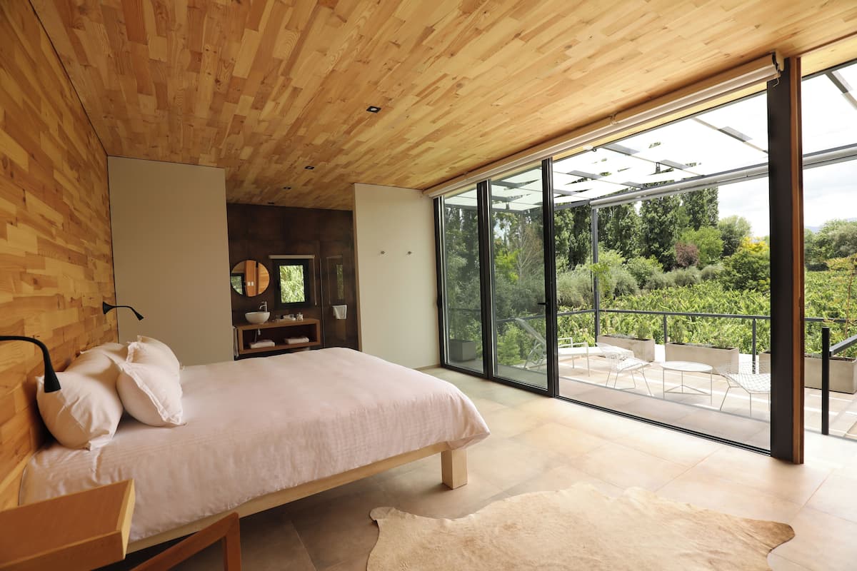 Ein modernes Schlafzimmer mit Holzboden, einem großen Bett und einer Glastür zu einer Terrasse mit Sitzgelegenheit.