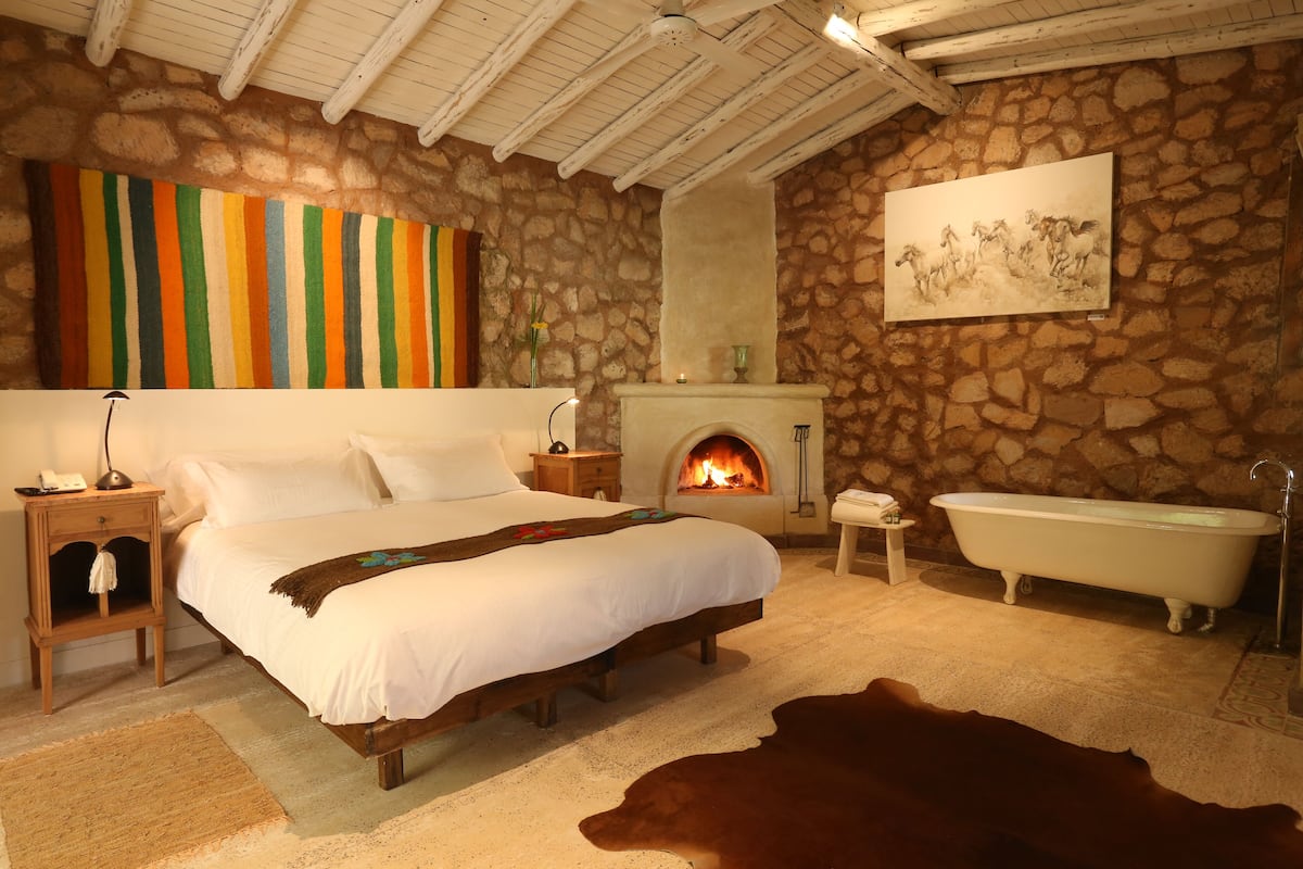 Ein Schlafzimmer mit Steinwand, Kamin, Bett, Nachttisch, Badewanne und einem Kuhfellteppich.