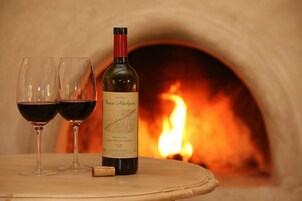 A bottle of wine and two glasses on a table with a fireplace in the background.