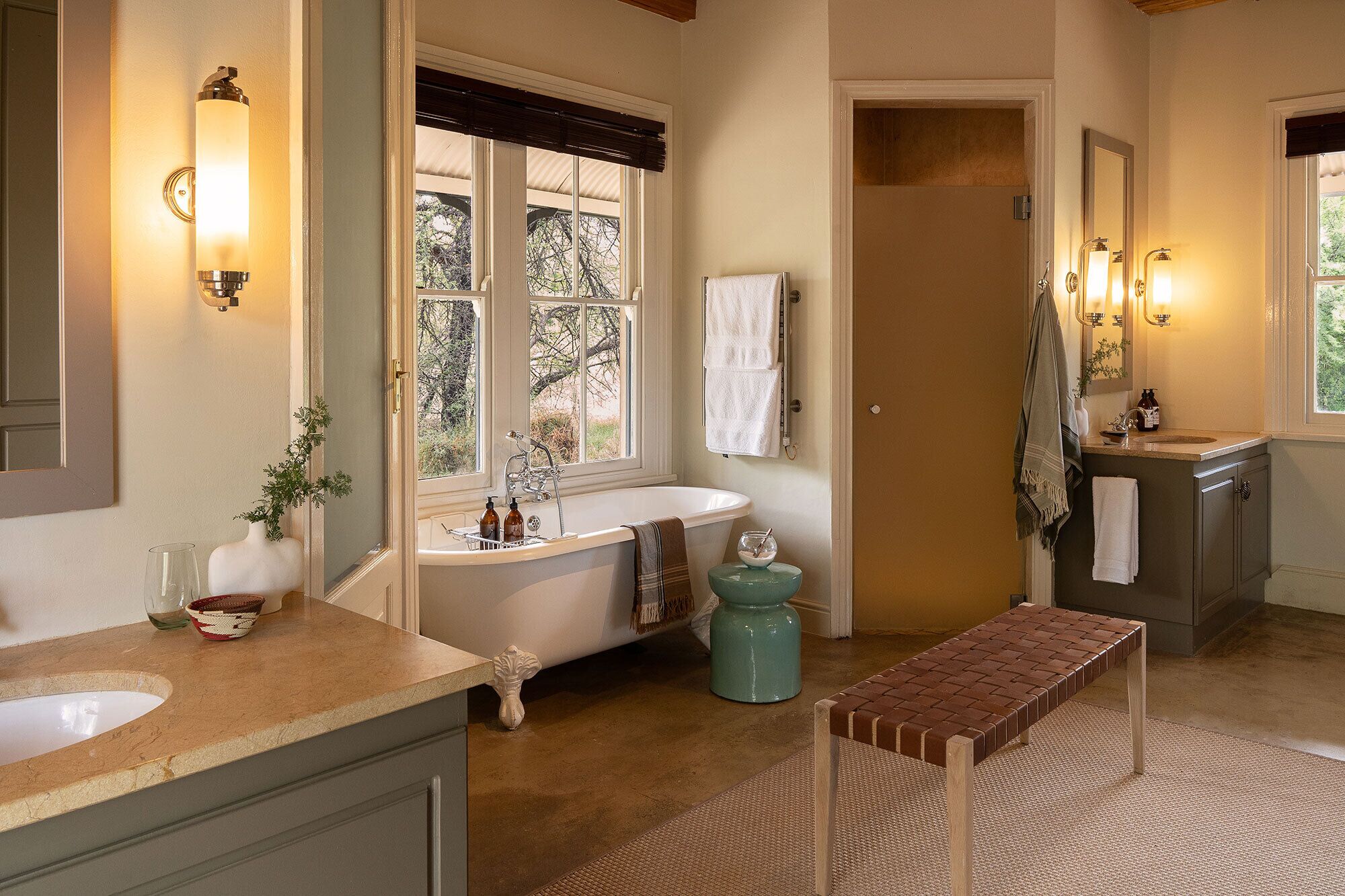 A bathroom with a bathtub, a sink, a mirror, and a bench.