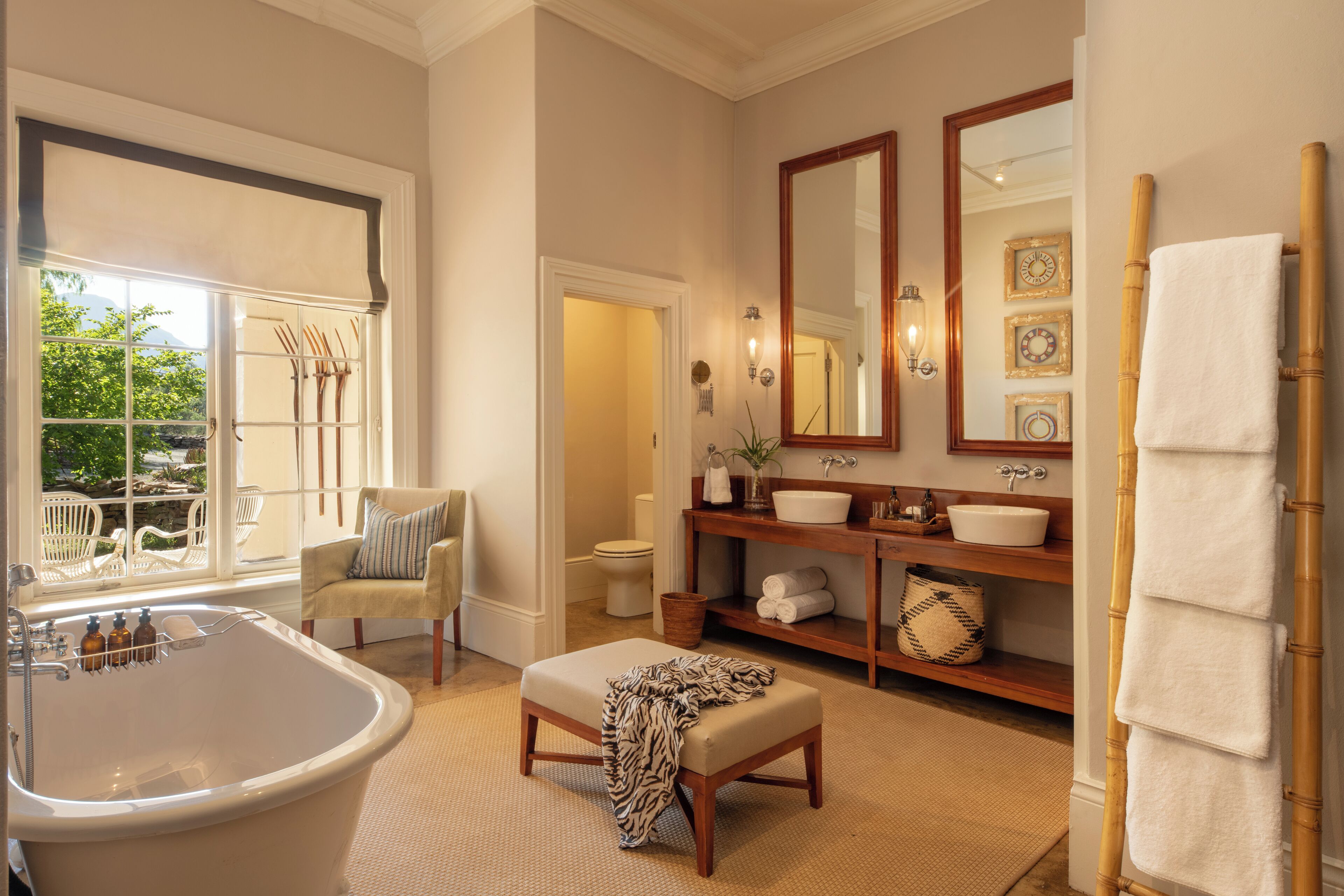 A spacious bathroom with a large bathtub, a vanity with a mirror, and a window offering a view of outdoor furniture.