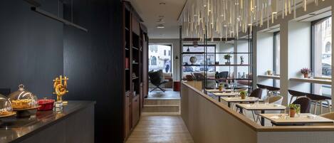 A modern hotel lobby with a long reception desk, seating area, and large windows offering views of the street.