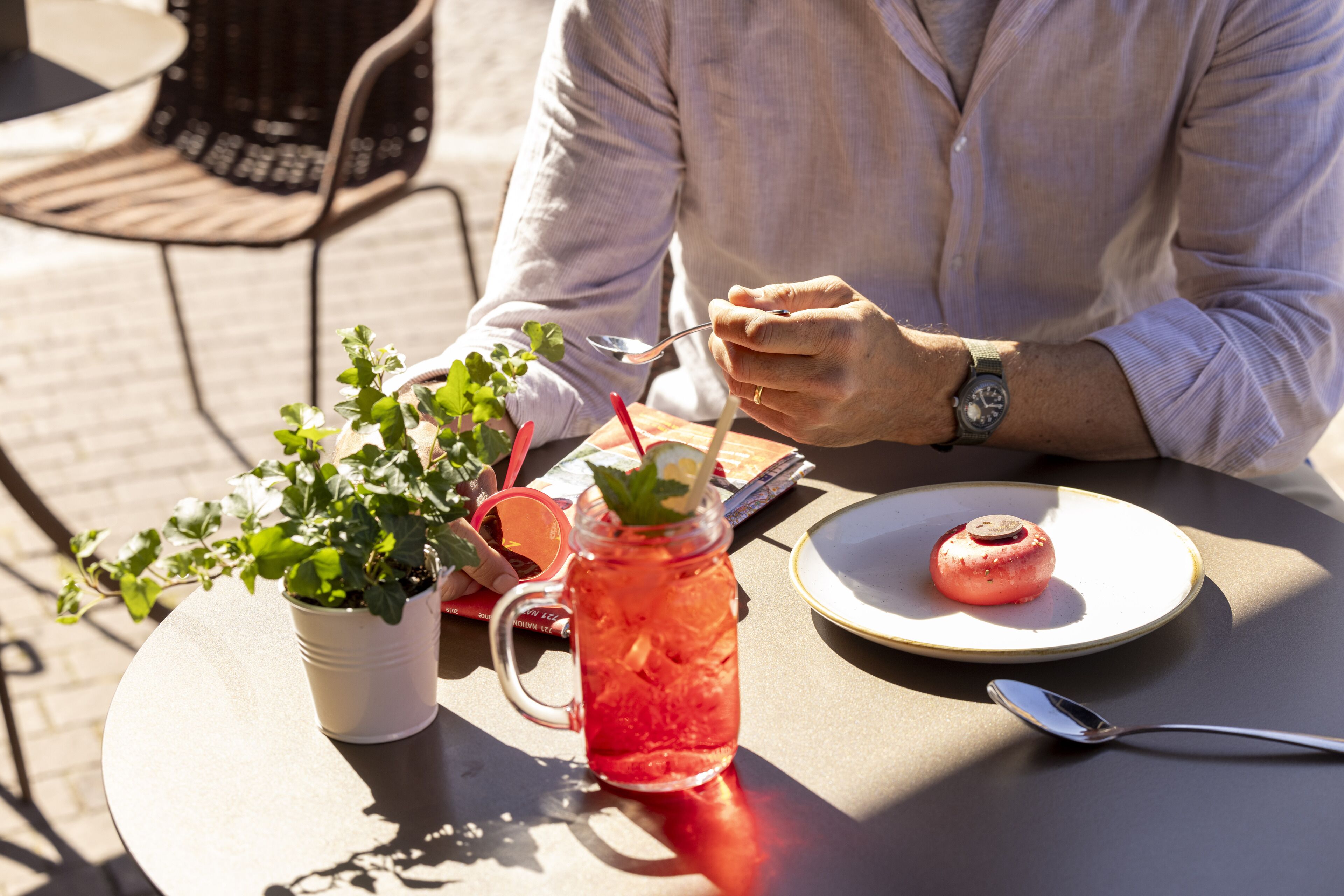 A person dining outdoors with a plate of food, a drink in a mason jar, and a potted plant on the table.