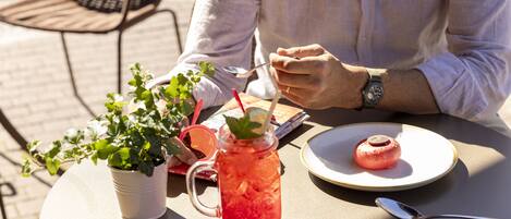 A person dining outdoors with a plate of food, a drink in a mason jar, and a potted plant on the table.