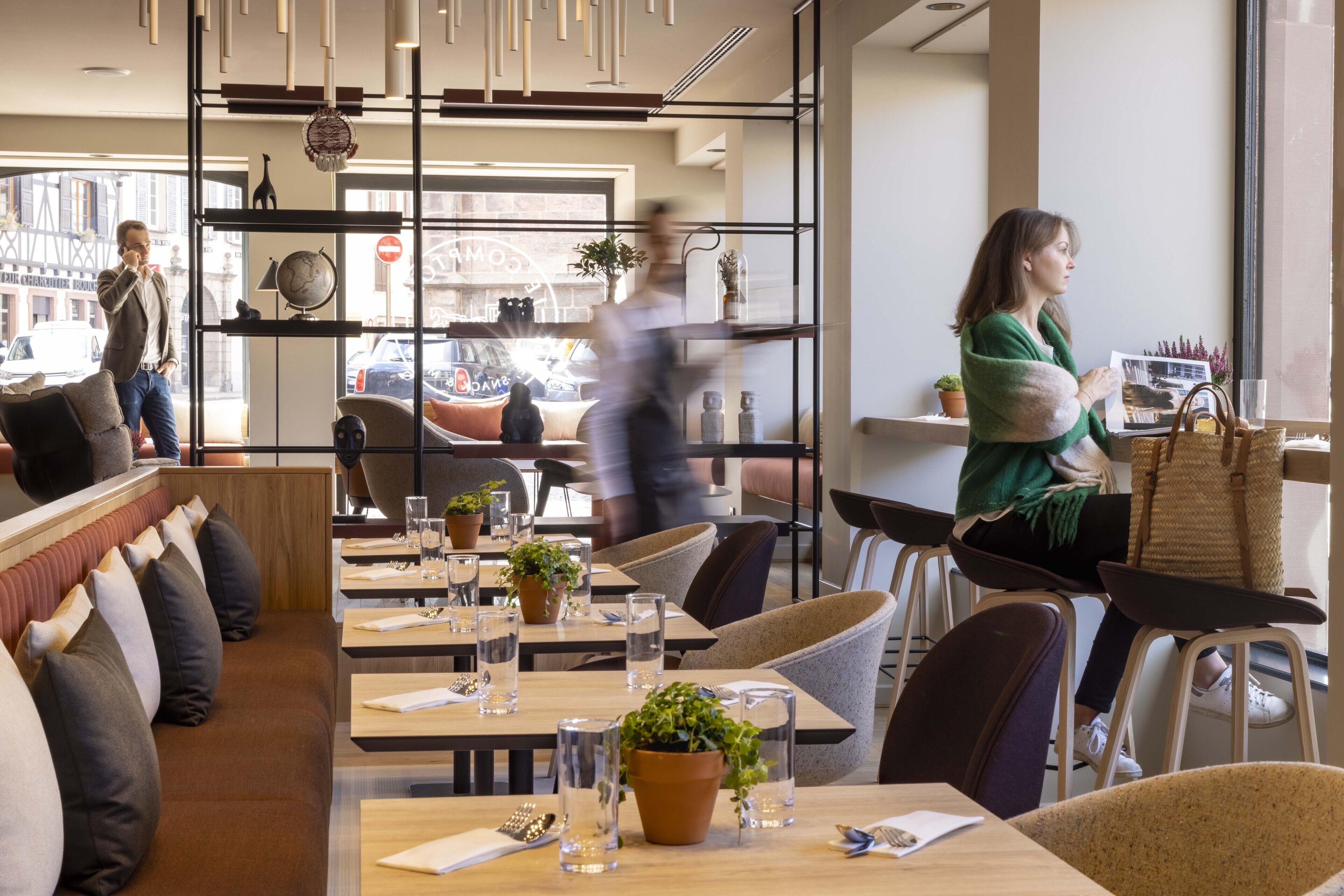 A modern restaurant with wooden tables, cushioned seating, and potted plants.