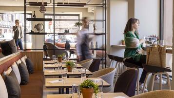 A modern restaurant with wooden tables, cushioned seating, and potted plants.