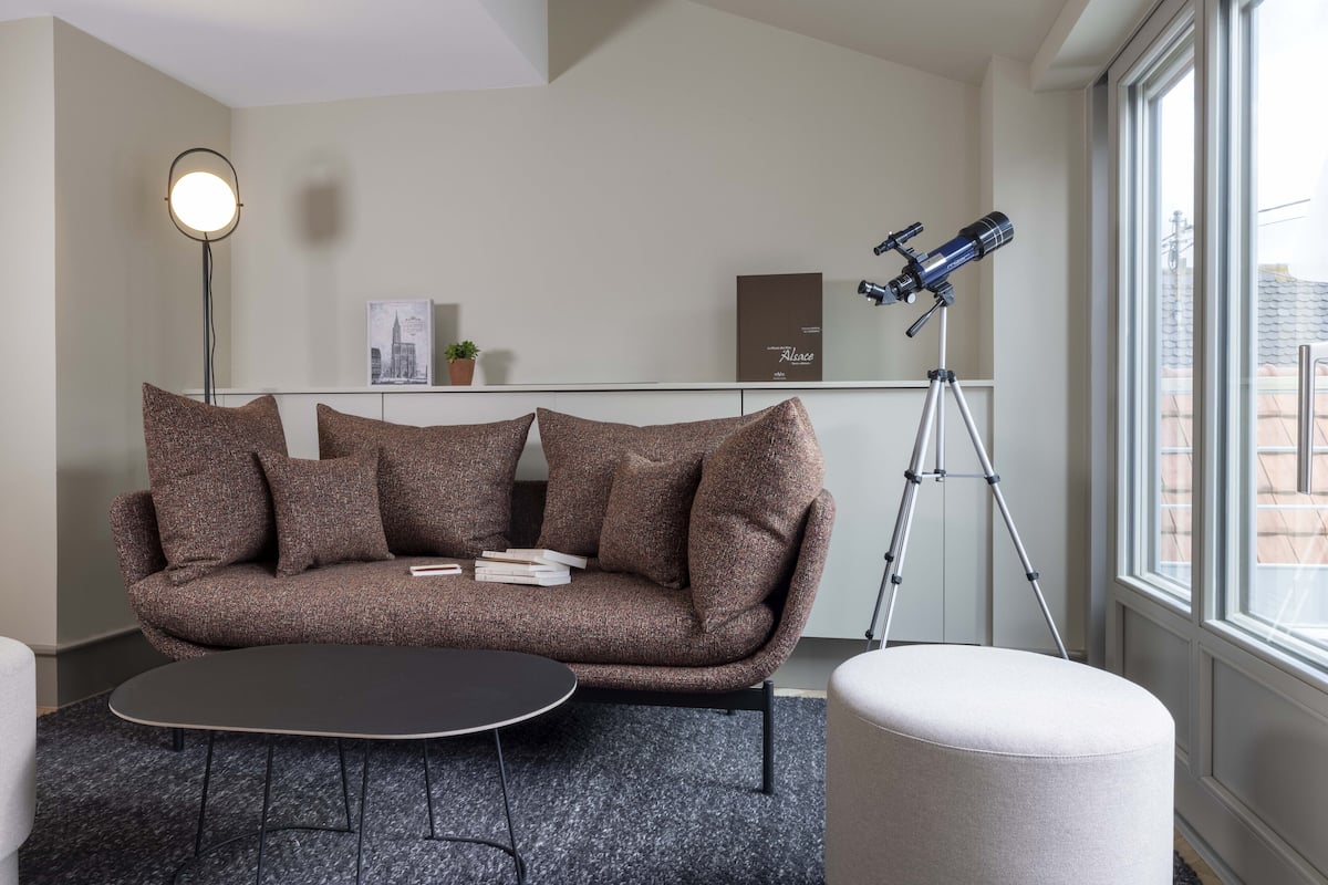 A modern living room with a brown sofa, a round coffee table, a floor lamp, and a telescope on a tripod.
