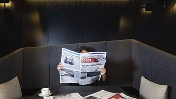 A person sitting in a dark, modern room with a sofa and a table. The person is holding a newspaper.