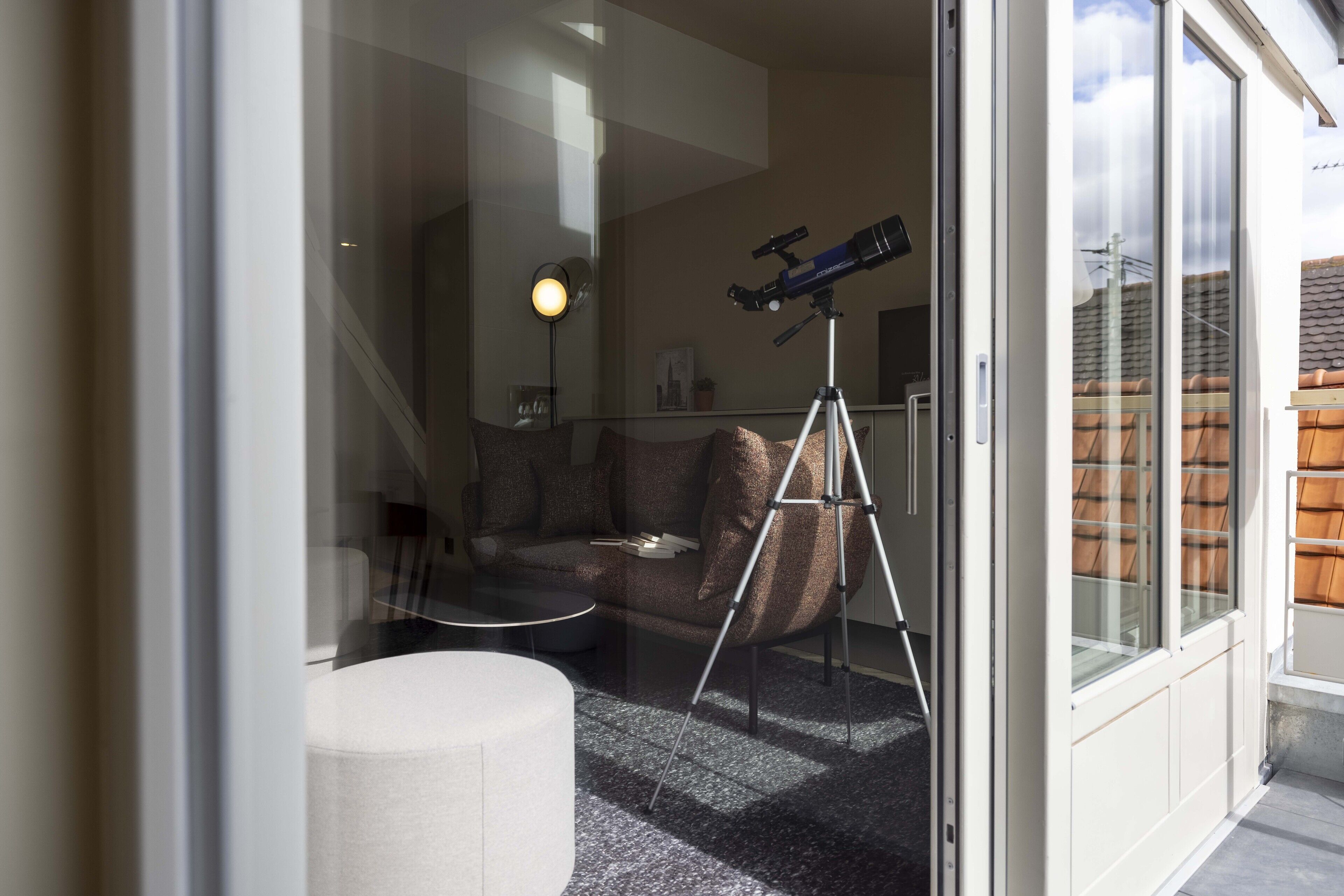 Una sala de estar moderna con un telescopio sobre un trípode, un taburete redondo y un sofá con cojines.