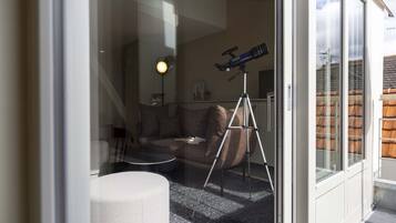 Una sala de estar moderna con un telescopio sobre un trípode, un taburete redondo y un sofá con cojines.