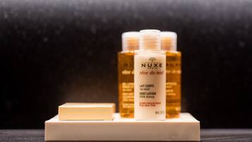 A display of NUXE body lotion bottles and a bar of soap on a marble surface.