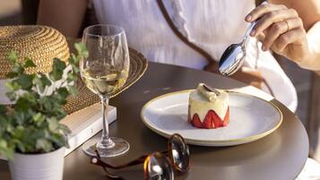 A dessert on a plate with a spoon, a glass of white wine, and a potted plant on a table.