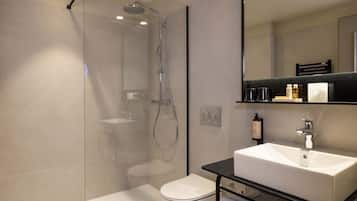 Un baño moderno con ducha envuelta en vidrio, inodoro blanco y encimera negra con lavabo blanco.
