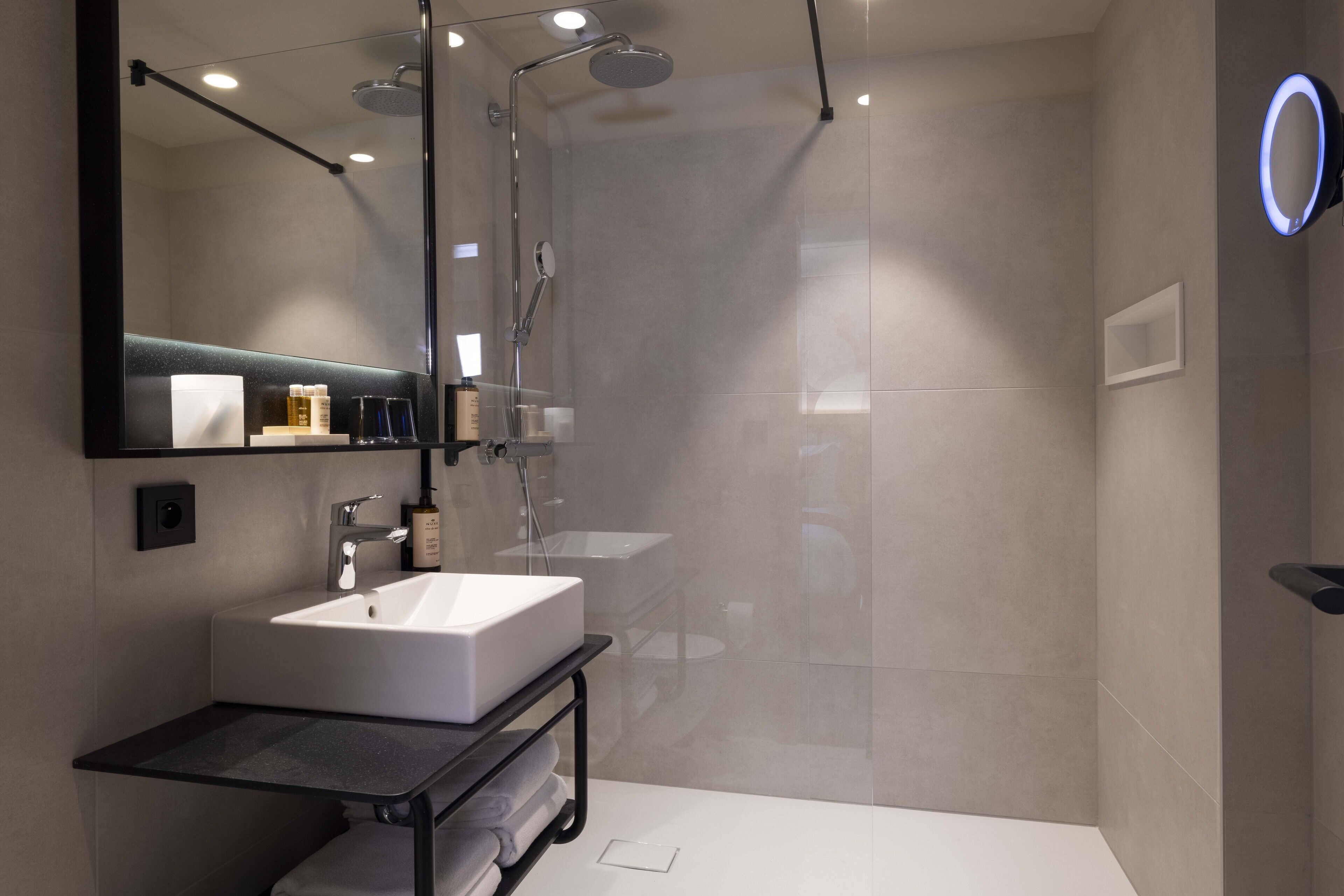 Un baño moderno con un espejo grande, un lavamanos blanco, una ducha y un tocador con encimera negra.