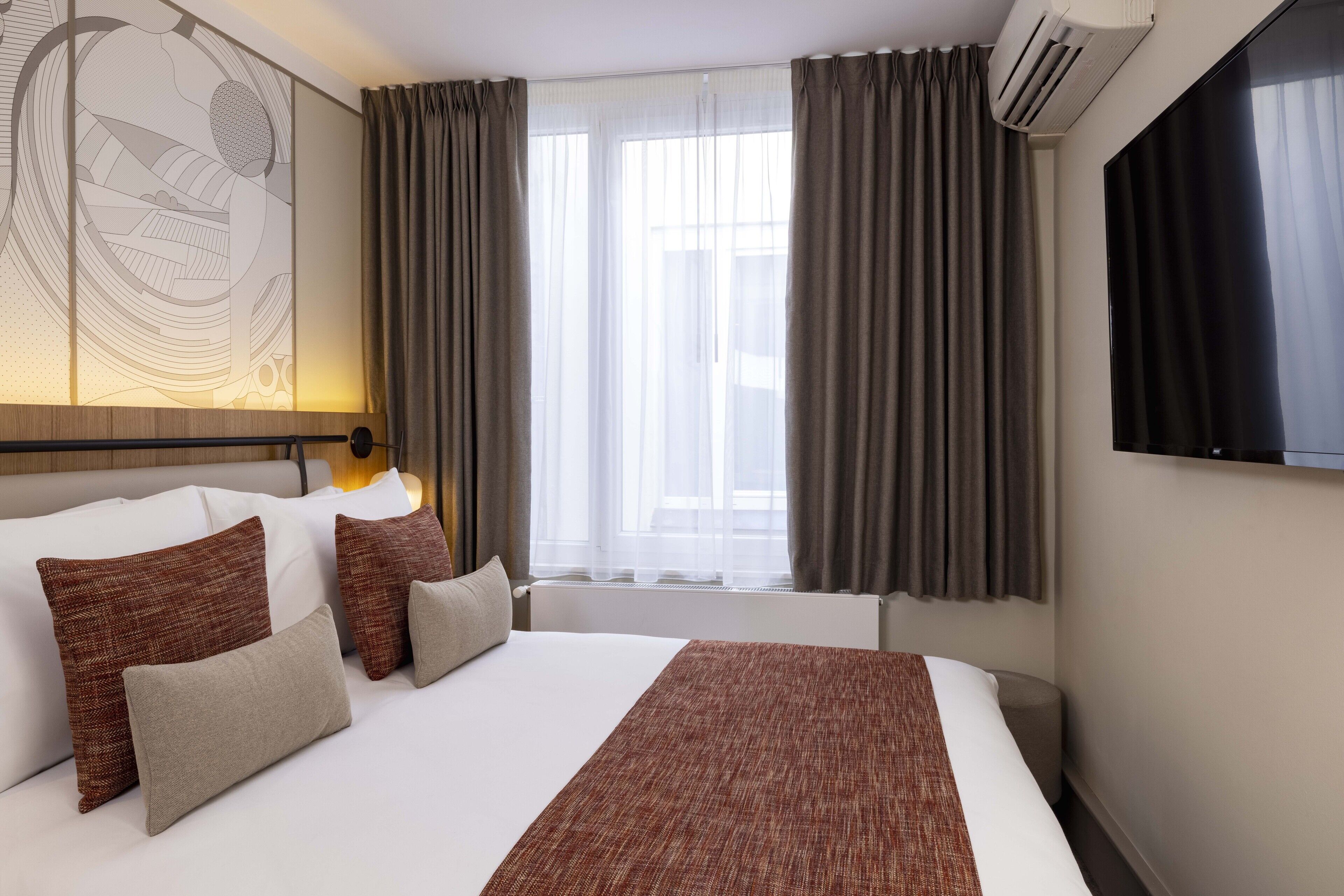 Een hotelkamer met een groot bed, een flatscreen televisie, een airconditioning en een raam met gordijnen.