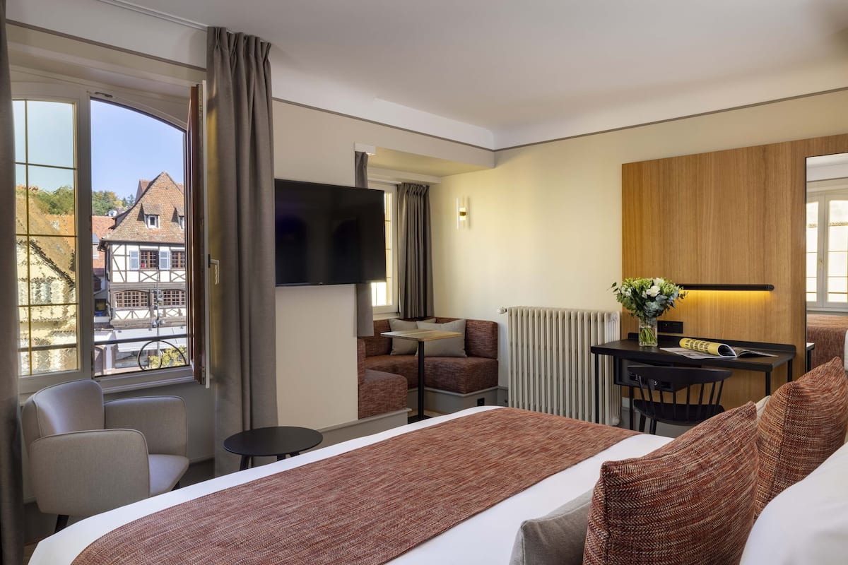 A hotel room with a large bed, a desk with a chair, a sofa, and a TV.