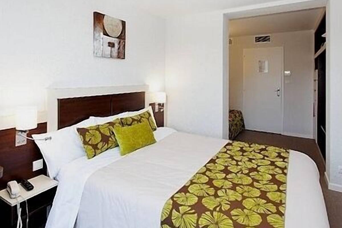 A hotel room with a large bed, a nightstand with a phone, and a door leading to another room.