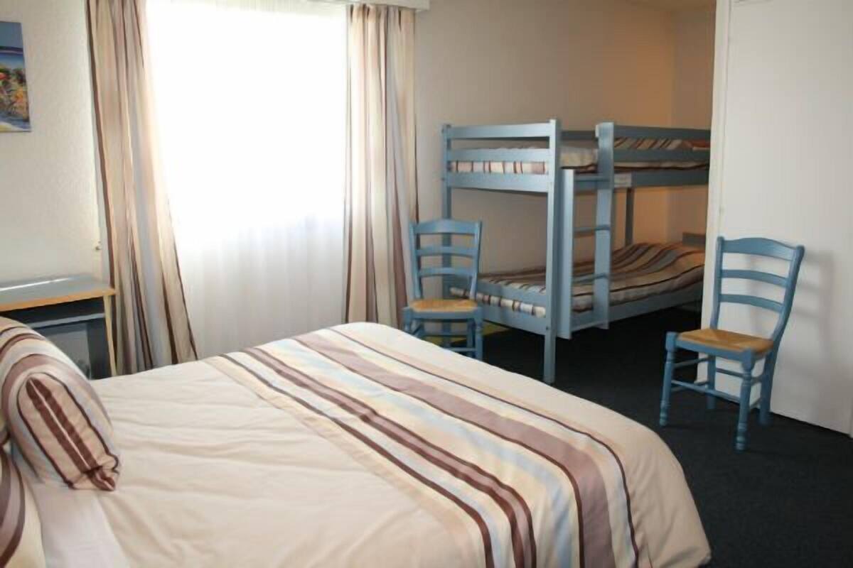 A room with a bunk bed, two chairs, a desk, and a bed with striped bedding.