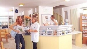 Aula, jossa on vastaanottotiski, tuoleja ja taustalla portaikko.