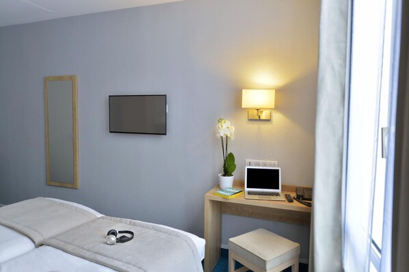 A hotel room with a bed, a desk with a laptop, a TV, a lamp, and a potted plant.