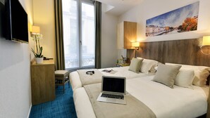 Habitación de hotel con cama, escritorio, computadora portátil, televisor y un cuadro en la pared.