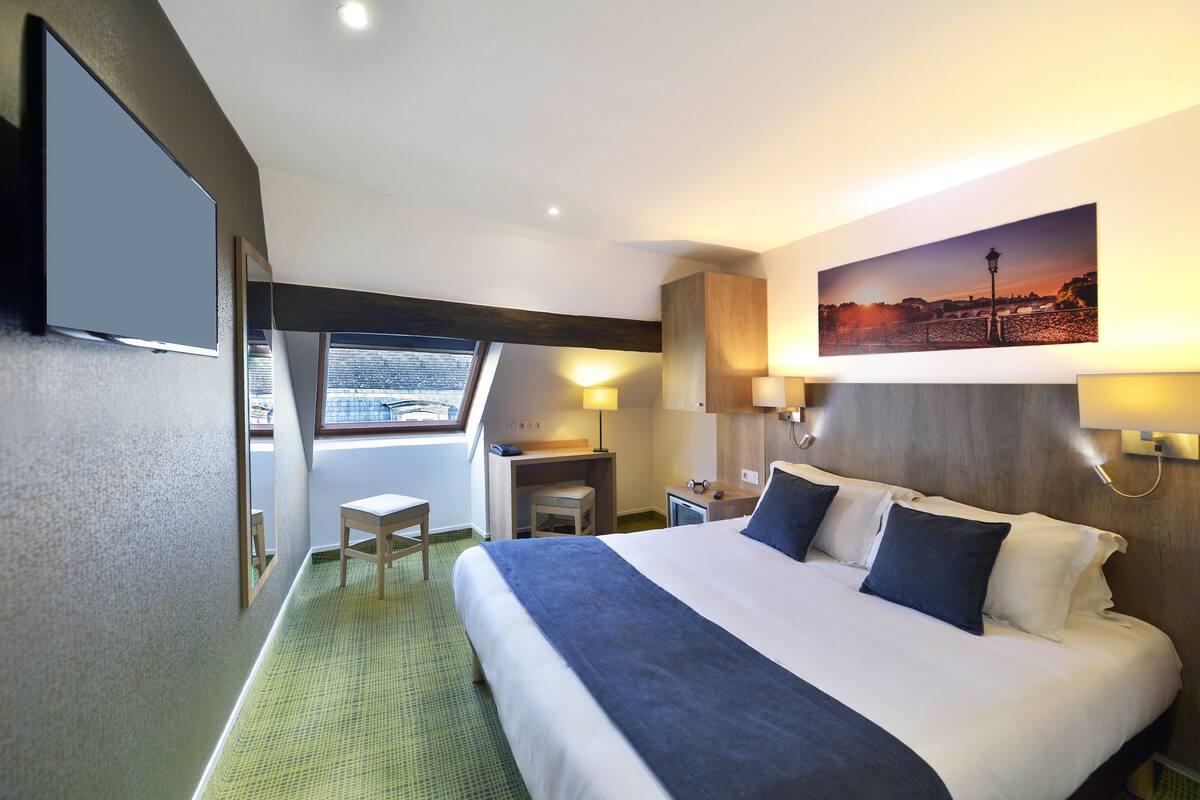 Une chambre d’hôtel avec un grand lit, un bureau, une chaise, une télévision et une fenêtre donnant sur un beau paysage.