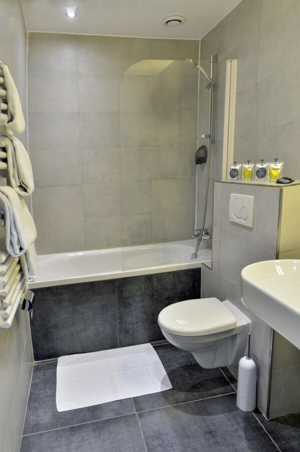A modern bathroom with a bathtub, toilet, and sink. - Hotel Eugenie (Paris)