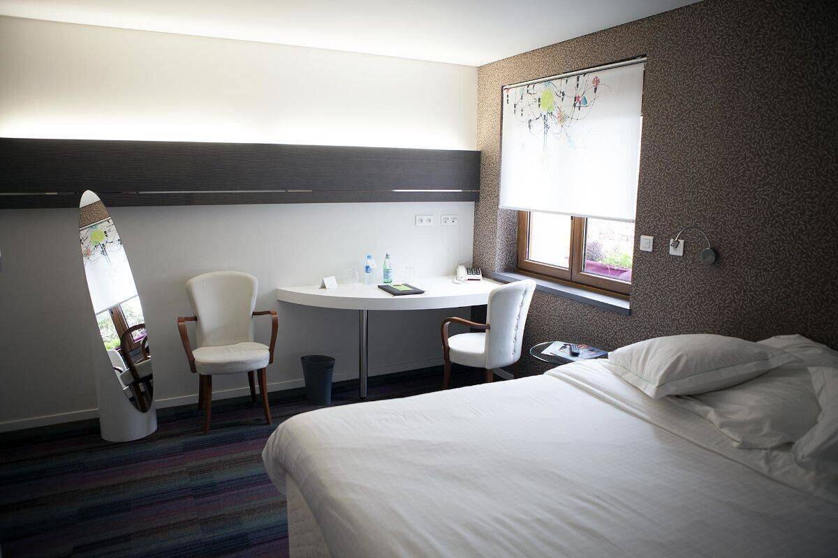 A hotel room with a bed, two chairs, a small table, a window, and a wall with a decorative panel.