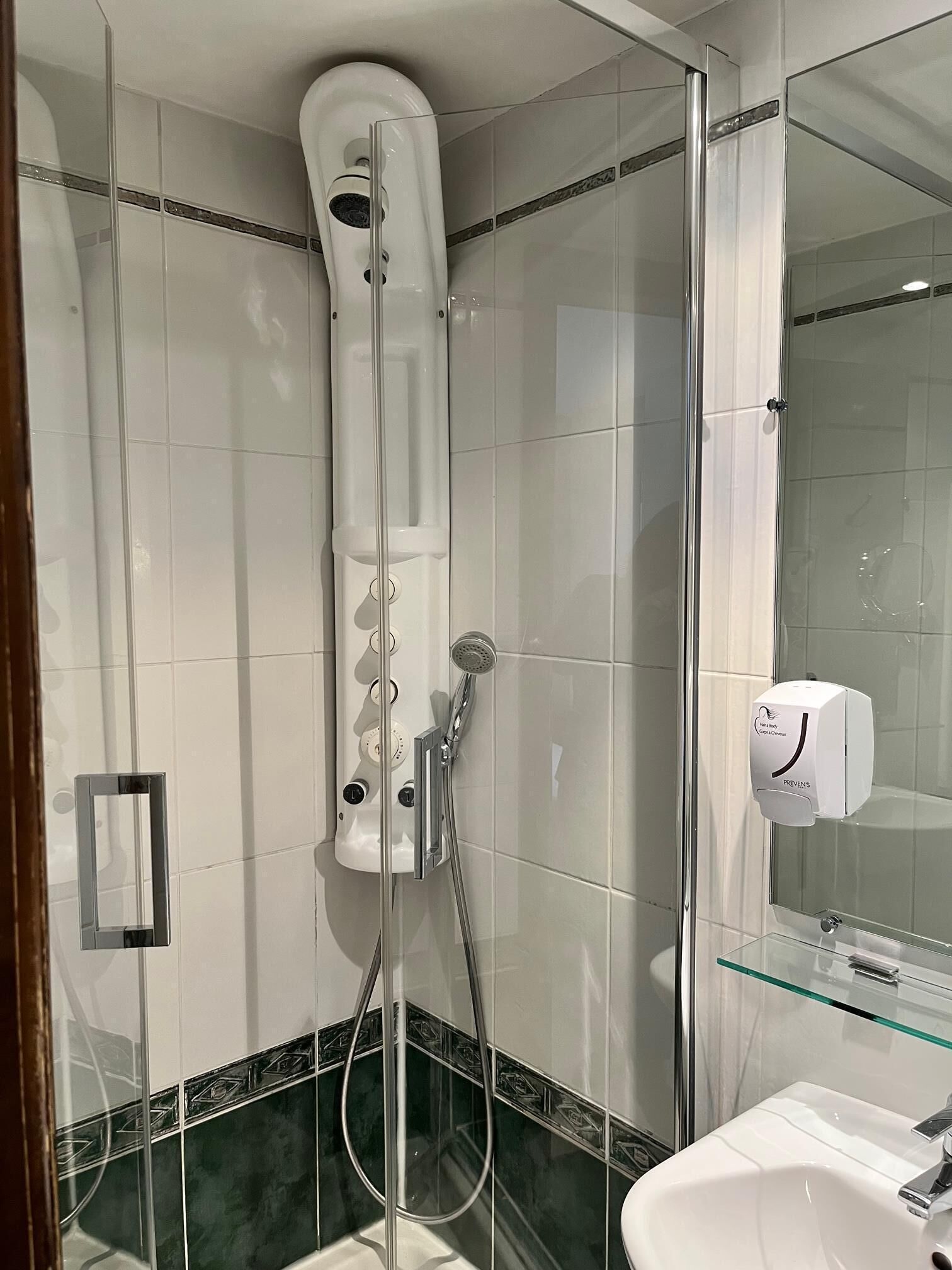 Une salle de bain moderne avec une douche à parois de verre, un lavabo blanc et un distributeur de savon liquide.