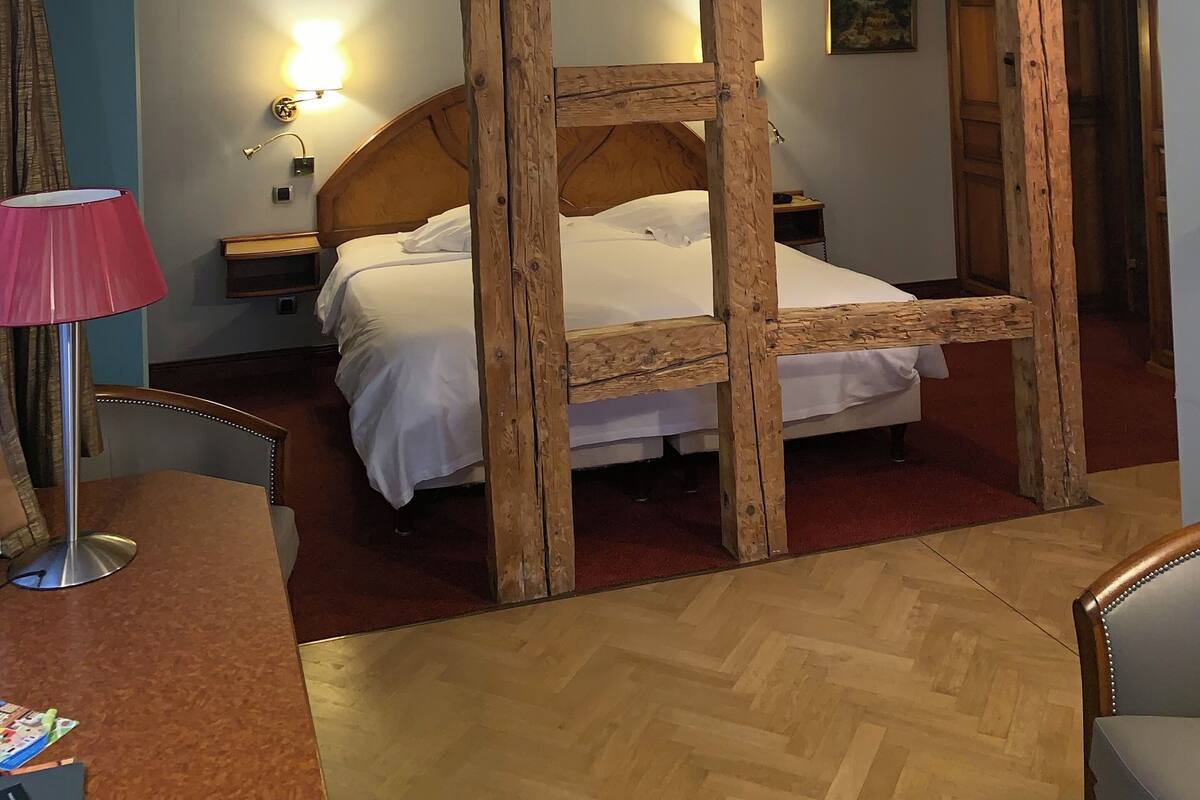 Ein Hotelzimmer mit einem Bettgestell aus Holz, einer roten Lampe, einem Nachttisch aus Holz, einem kleinen Tisch und einem roten Teppich.