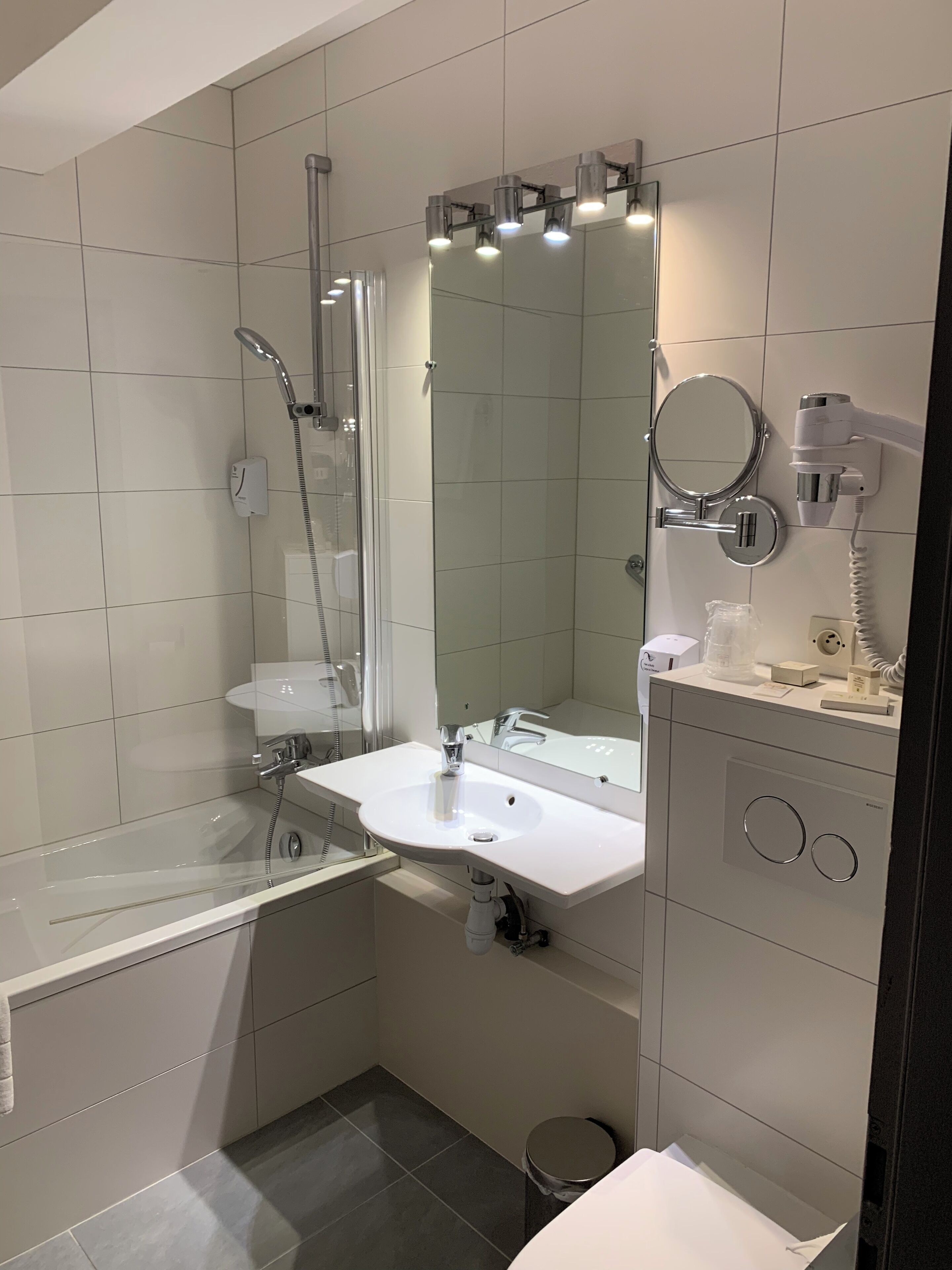 A modern bathroom with a glass-enclosed shower, a white sink, a large mirror, and a toilet.