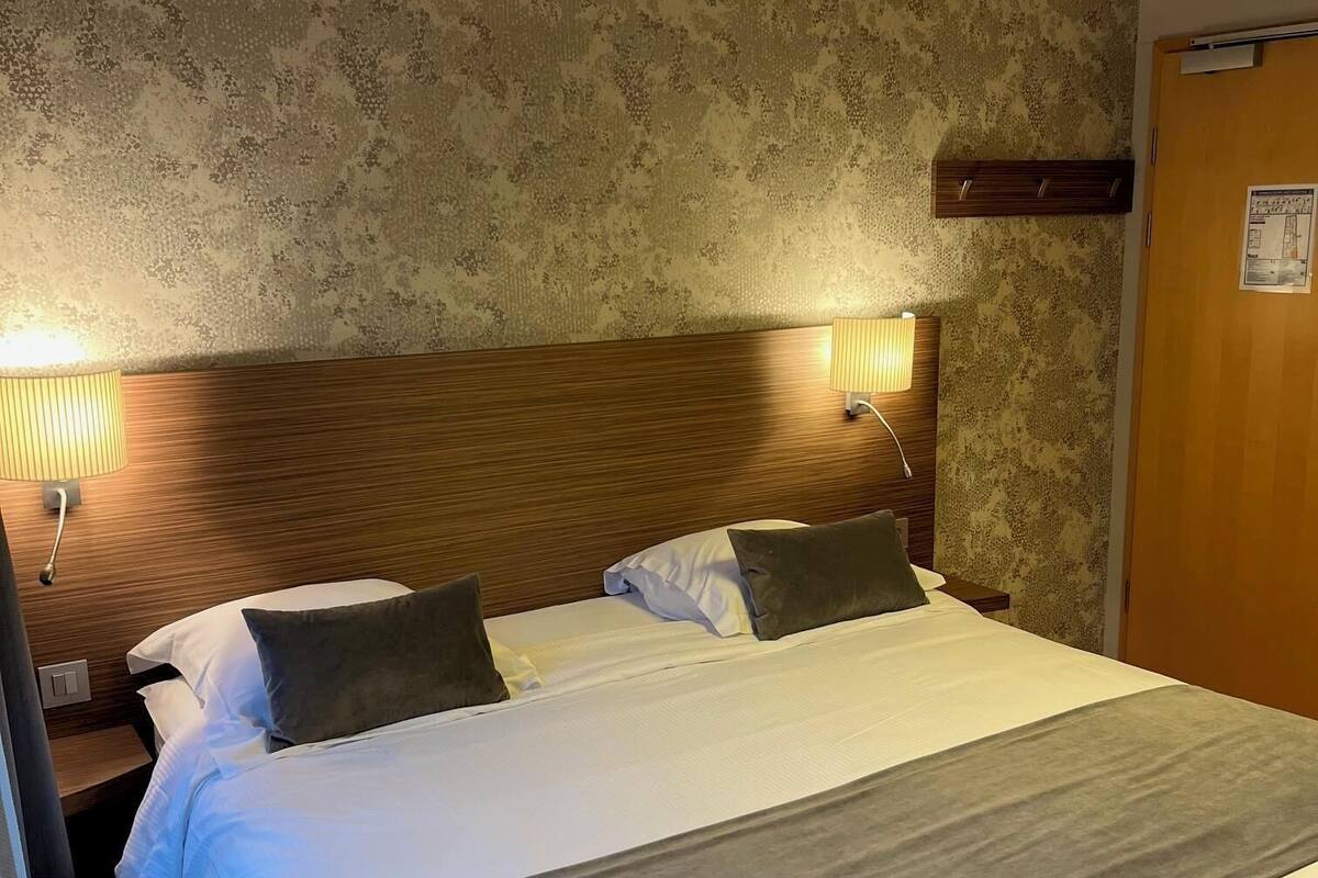 Ein Hotelzimmer mit einem großen Bett, zwei Nachttischlampen, einem Holz-Kopfteil und einer Wand mit Muster.