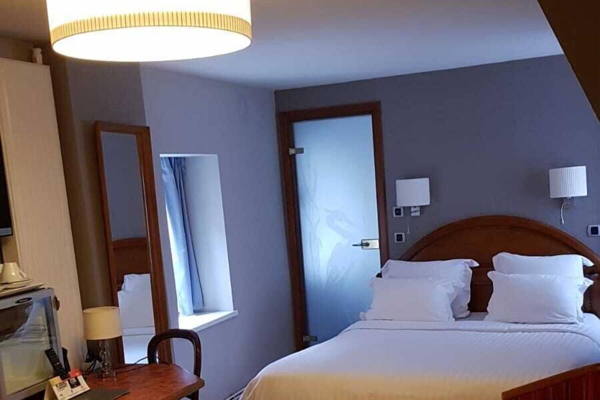 Ein Hotelzimmer mit Bett, Schreibtisch, Stuhl, Lampe und einem großen Fenster.