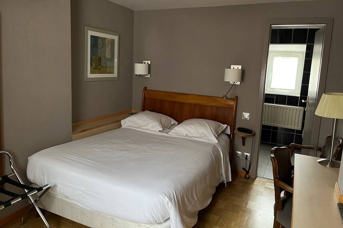 Ein Hotelzimmer mit einem großen Bett, Nachttischen, einem Schreibtisch mit Stuhl, einem Fenster und einer Tür.