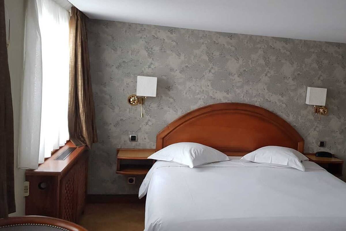 Ein Hotelzimmer mit einem großen Bett, zwei Nachttischen, einem Schreibtisch und einem Fenster mit Vorhängen.