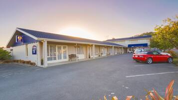 Ein Motel mit einer Reihe von Zimmern, einem Parkplatz und einem roten Auto vor der Einfahrt.
