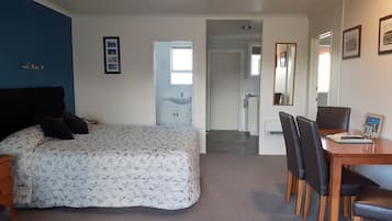 A bedroom with a bed, a desk with chairs, a mirror, and a bathroom visible through an open door.