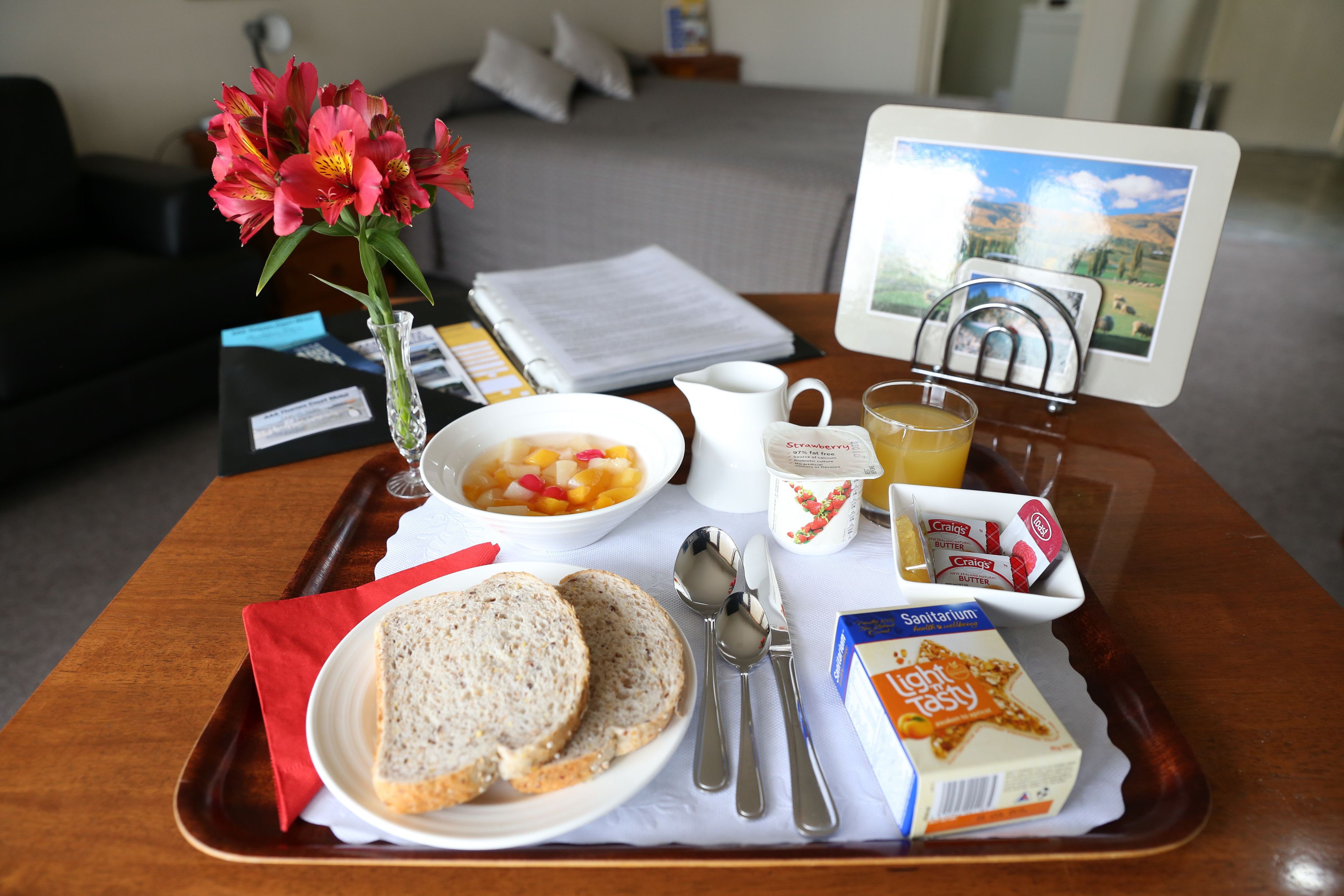 A breakfast tray with bread, a bowl of fruit, a cup of coffee, a glass of juice, and a box of cereal.