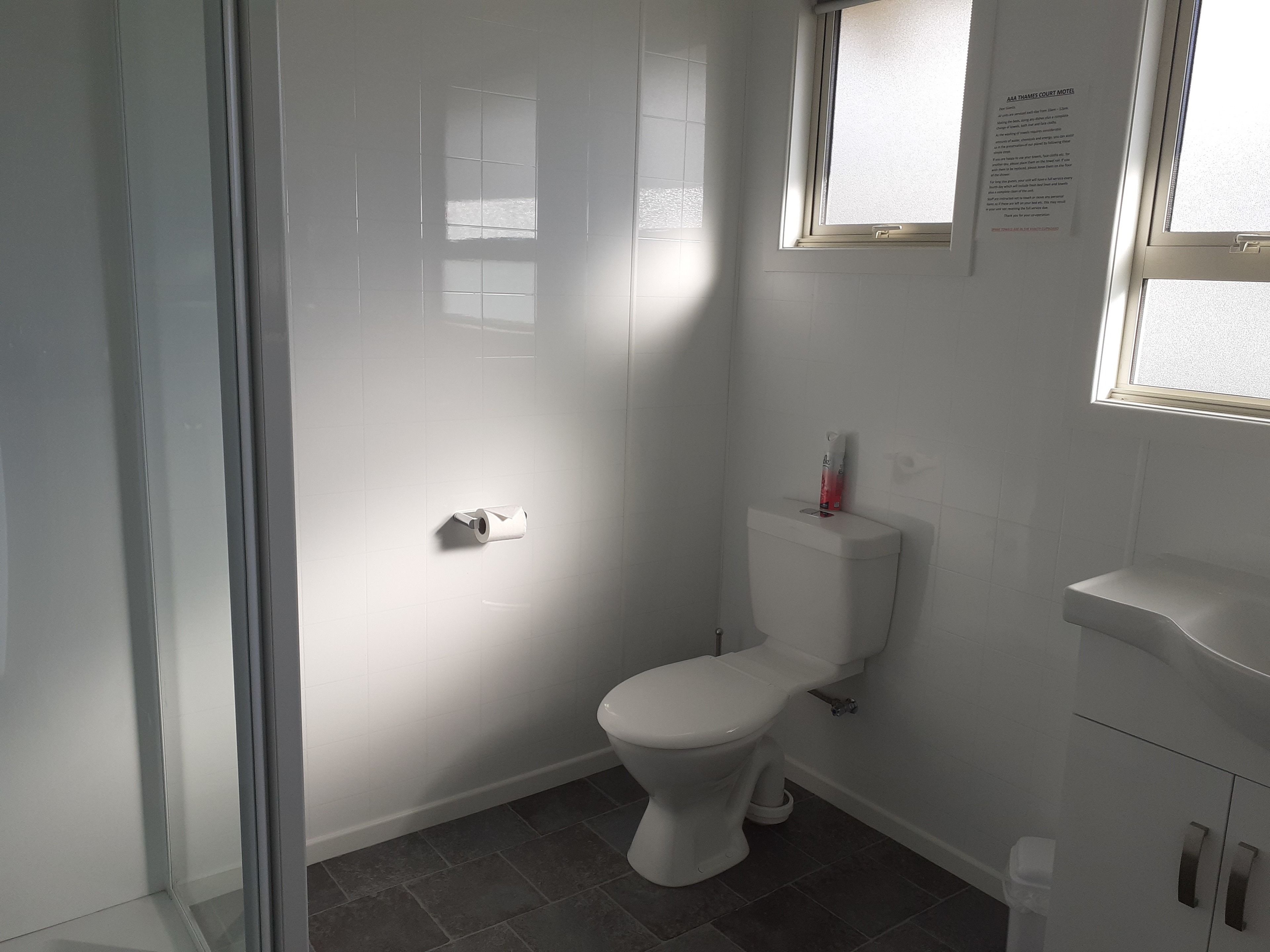 A bathroom with a toilet, a window, and a paper towel dispenser.