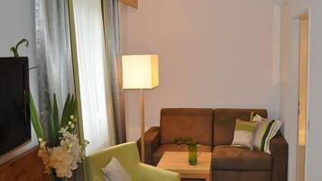Una sala de estar con un sillón verde, un sofá marrón, una mesita de noche con una lámpara y un televisor a la izquierda.