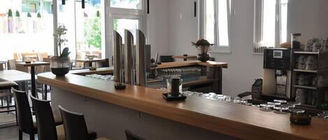 Un área de bar moderna con mostrador de madera, taburetes y una máquina de café.