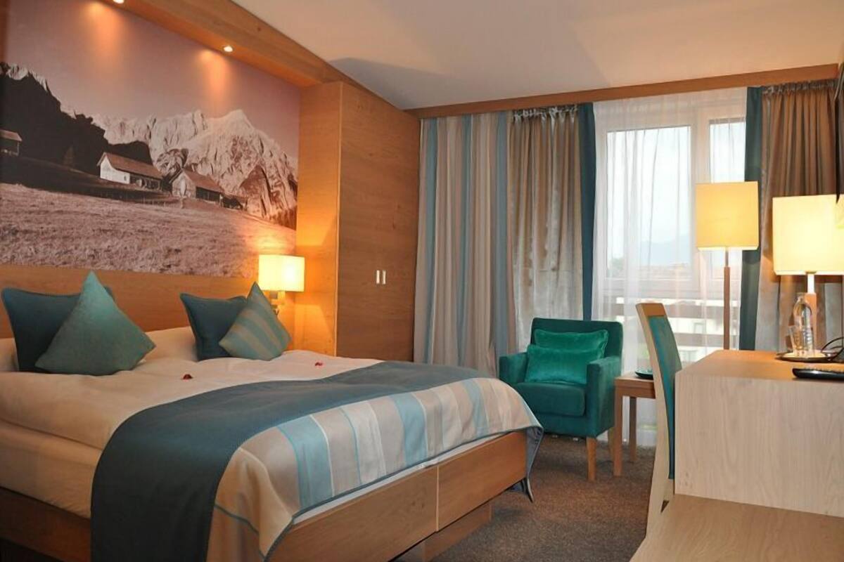 A hotel room with a large bed, a desk, a chair, and a window with curtains.