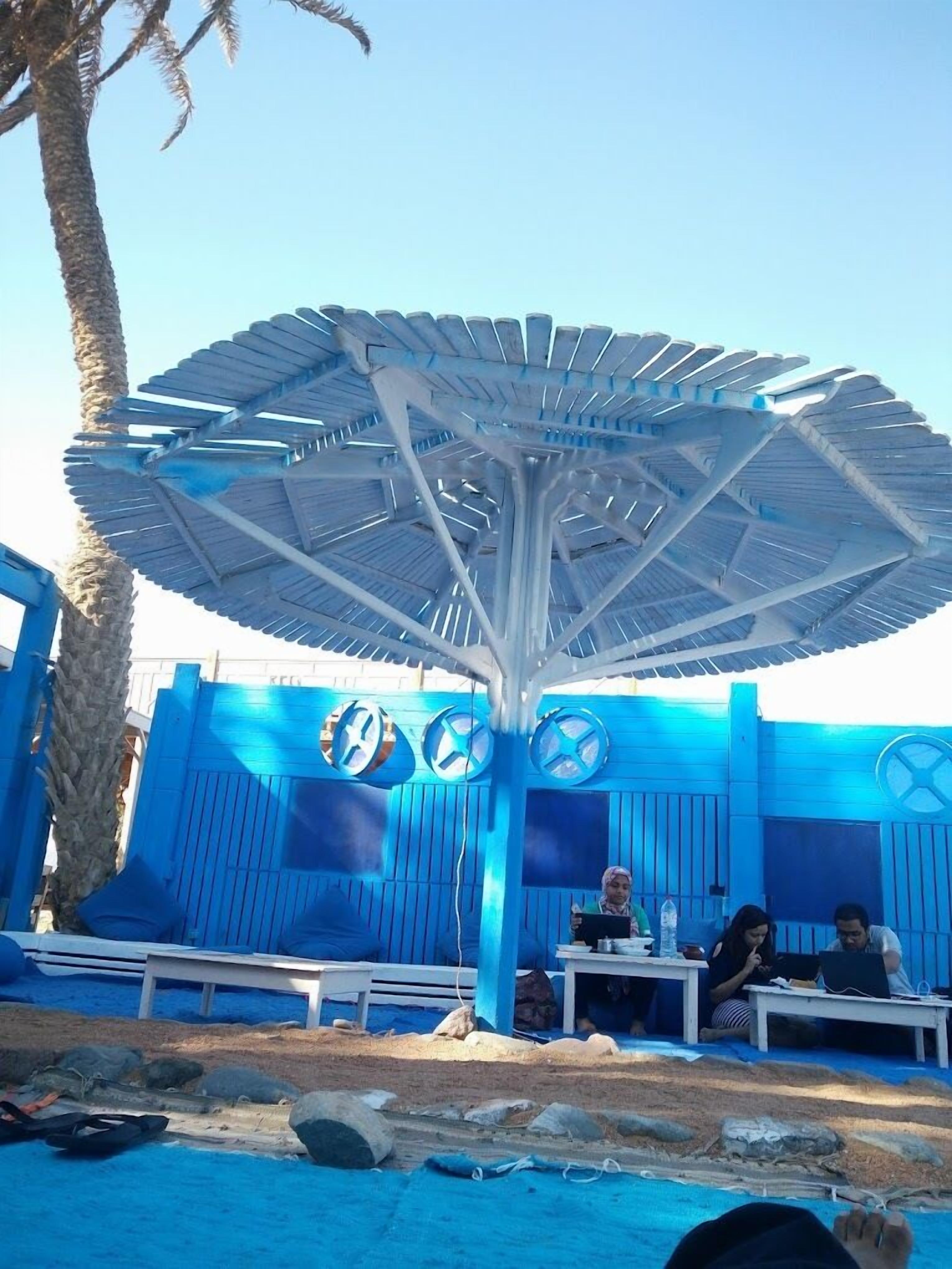 Un espace extérieur aménagé avec des sièges, un grand parasol, des murs bleus et des palmiers.