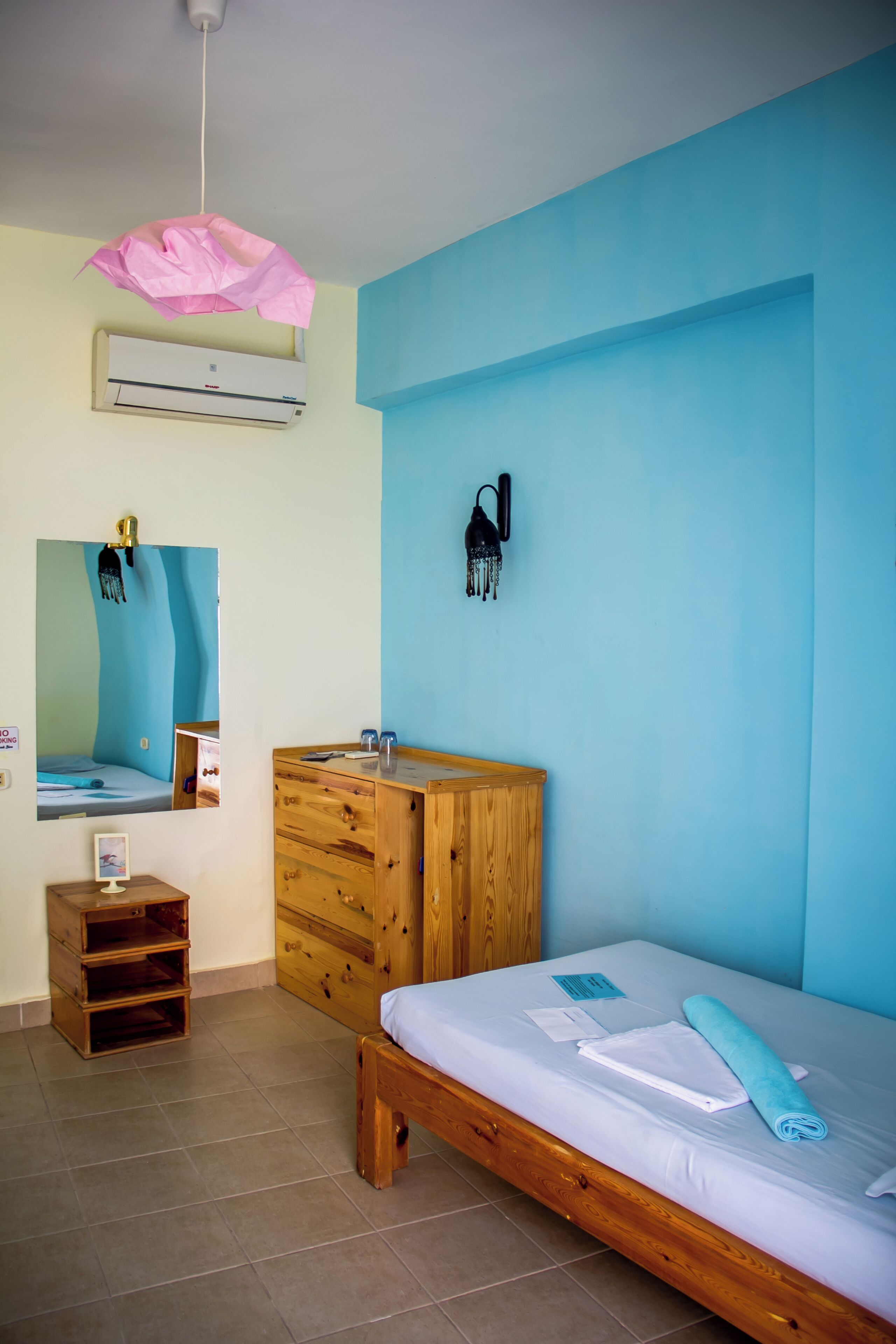 A bedroom with a wooden bed, a wooden dresser, a mirror, an air conditioning unit, and a wall-mounted light fixture.