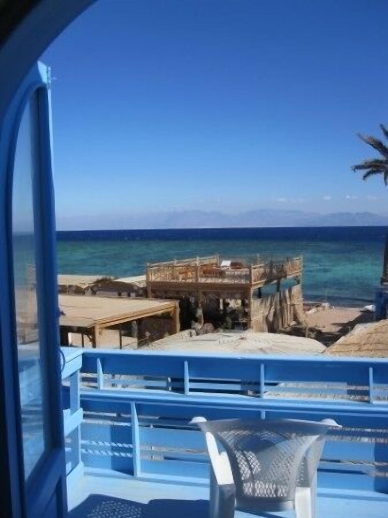 Une vue depuis un balcon donnant sur une plage, avec une structure en bois et un ciel d’un bleu limpide.
