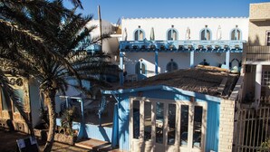 Un bâtiment à la façade bleue, doté d’un toit de chaume et surmonté d’un palmier en premier plan.