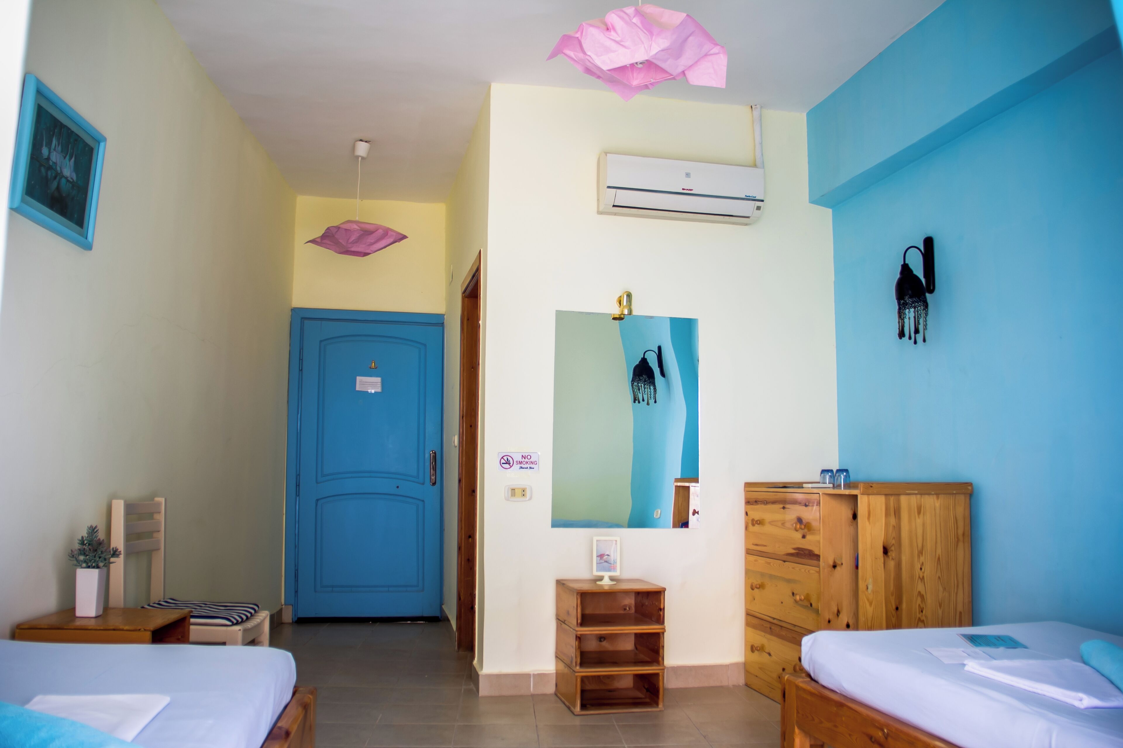 A room with two beds, a wooden dresser, a blue door, and a wall-mounted air conditioner.